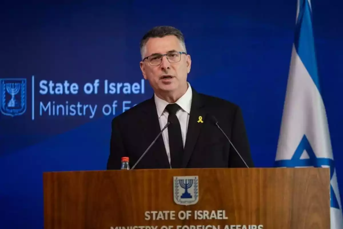Hombre con gafas y traje oscuro hablando en un podio del Ministerio de Asuntos Exteriores de Israel con una bandera israelí al fondo Hombre con gafas y traje oscuro hablando en un podio del Ministerio de Asuntos Exteriores de Israel con una bandera israelí al fondo