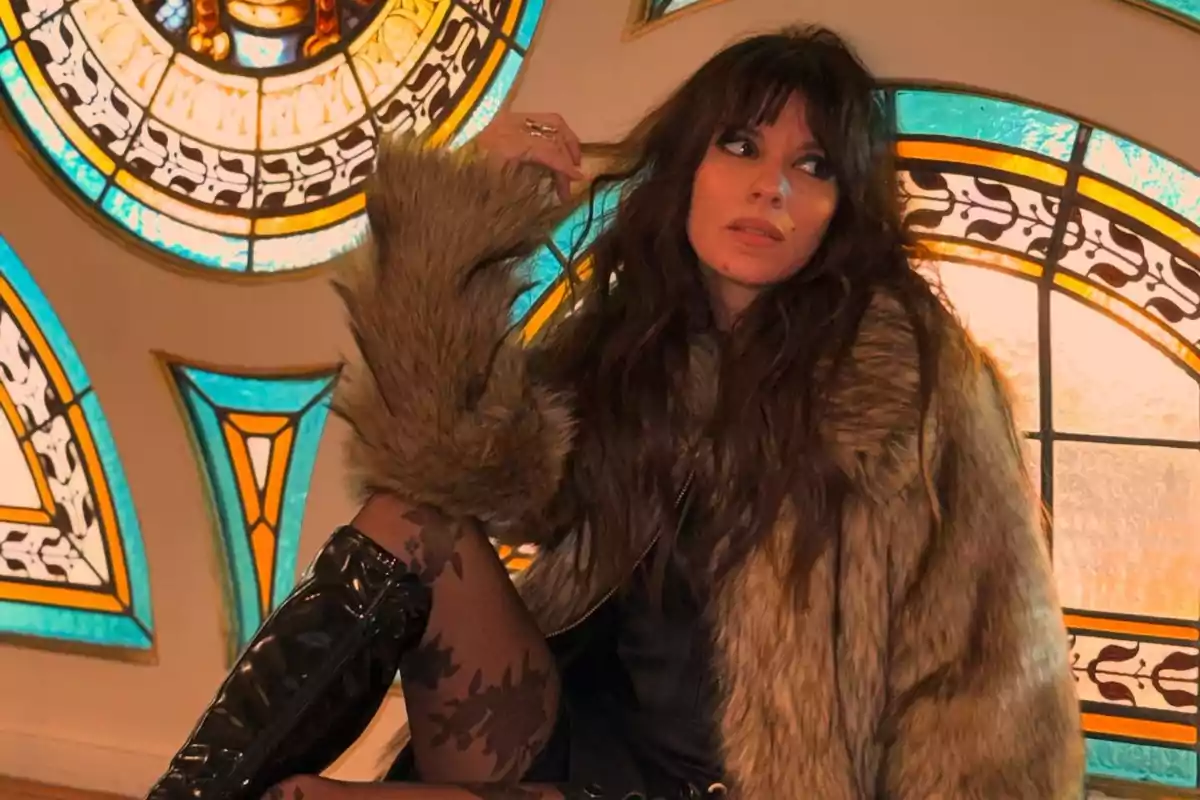 Woman in a faux fur coat and black boots sitting in front of colorful stained glass windows