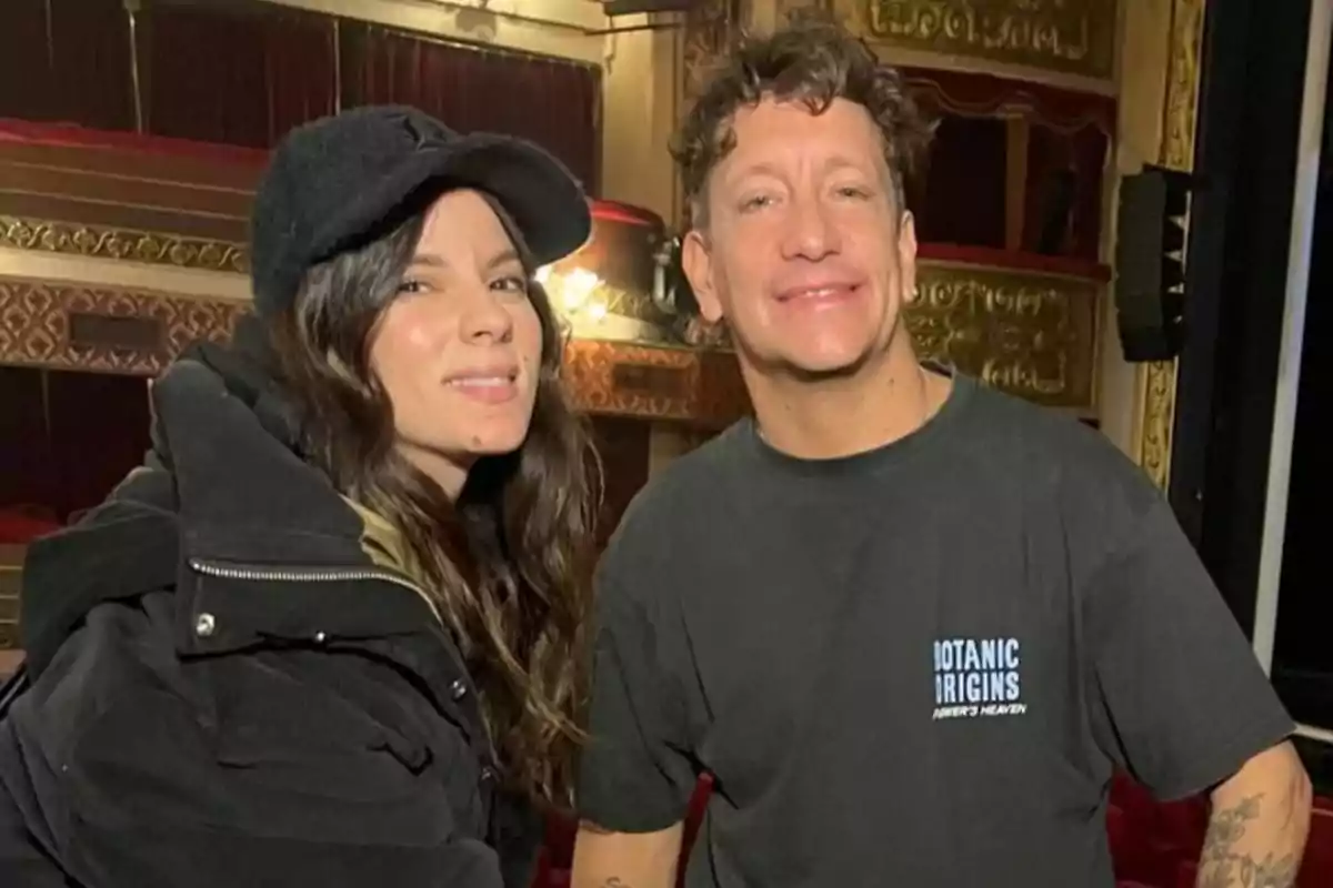 Dos personas posan sonrientes en el interior de un teatro con decoraciones doradas y cortinas rojas. Dos personas posan sonrientes en el interior de un teatro con decoraciones doradas y cortinas rojas.