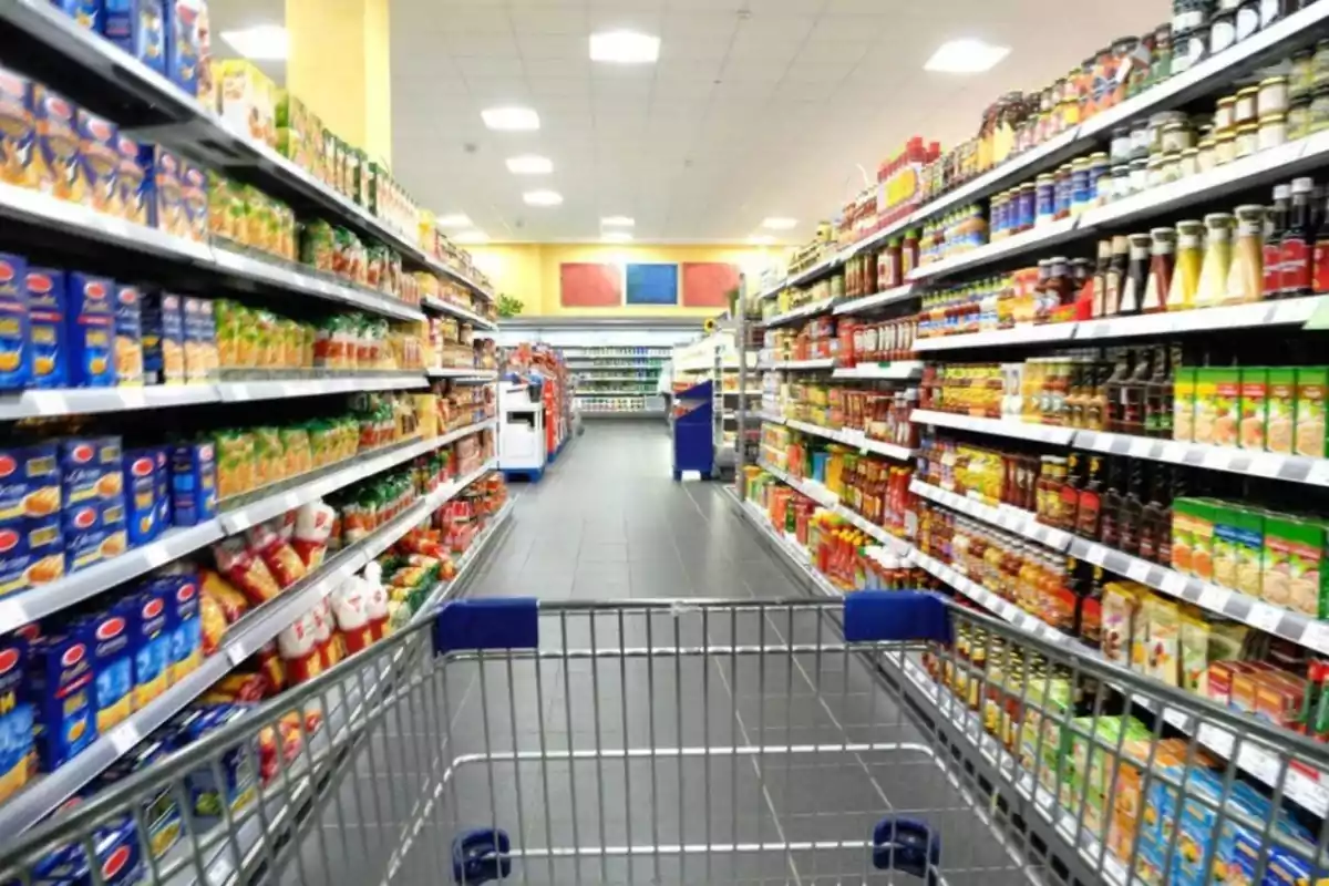 Pasillo de supermercado con estantes llenos de productos y un carrito de compras en primer plano