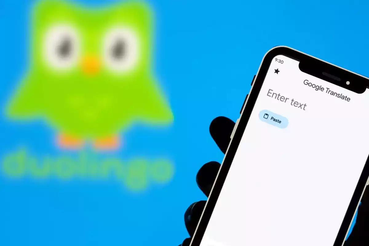 Una mano sostiene un teléfono con la aplicación de Google Translate abierta y al fondo se ve el logo borroso de Duolingo. Una mano sostiene un teléfono con la aplicación de Google Translate abierta y al fondo se ve el logo borroso de Duolingo.