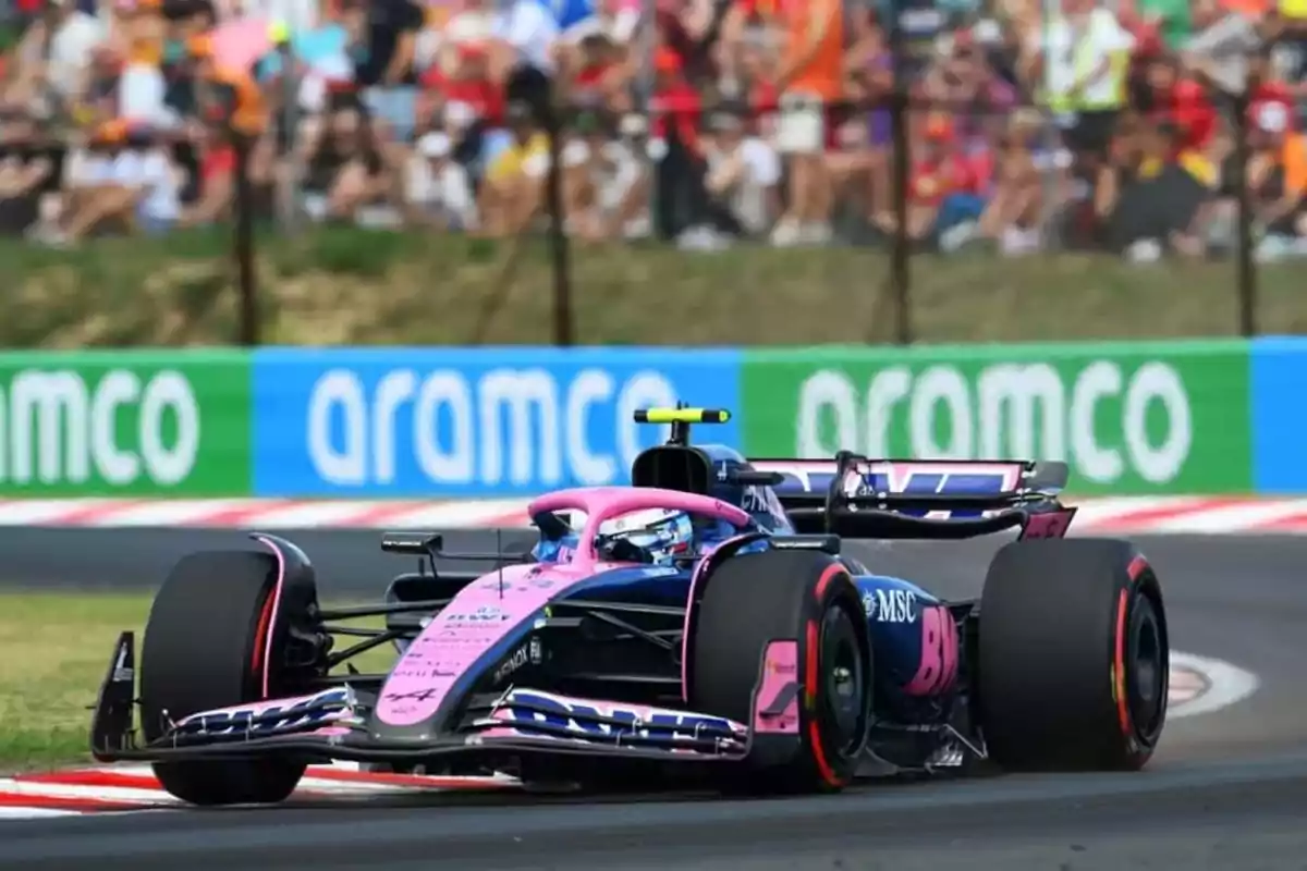 Pink and blue Formula 1 car racing on a track with spectators and Aramco advertisements in the background
