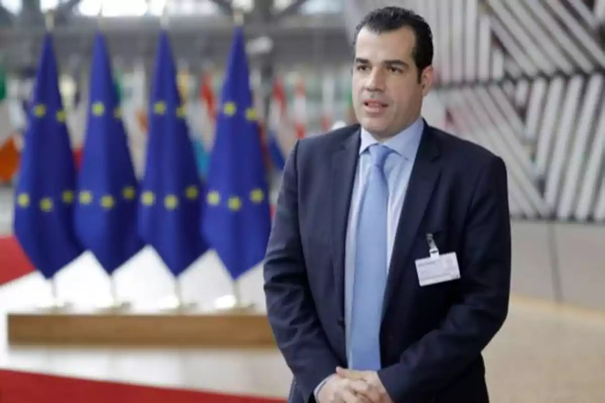 Hombre de traje y corbata posando en un recinto oficial con varias banderas de la Unión Europea al fondo Hombre de traje y corbata posando en un recinto oficial con varias banderas de la Unión Europea al fondo