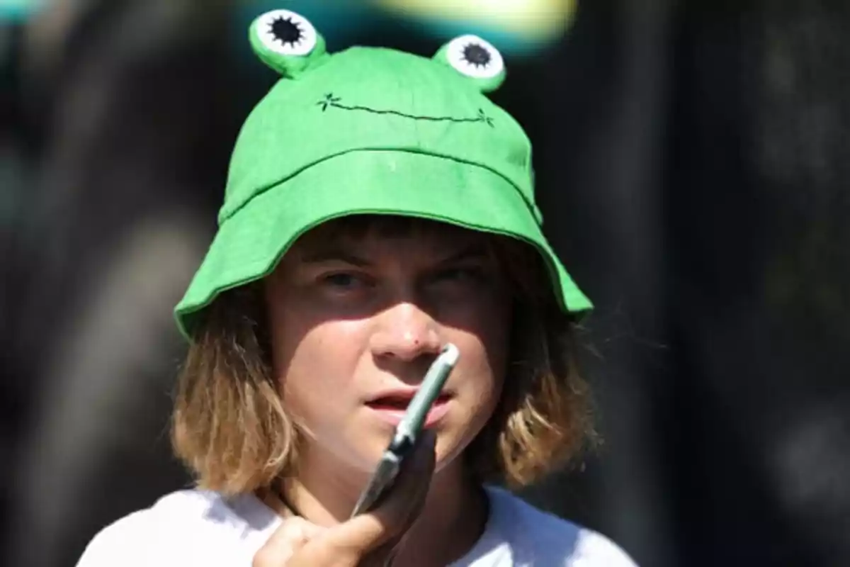 Persona con sombrero verde de rana sosteniendo un objeto cerca de su boca