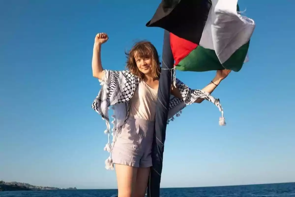 Mujer joven con el puño en alto junto a una bandera palestina en la playa bajo un cielo despejado Mujer joven con el puño en alto junto a una bandera palestina en la playa bajo un cielo despejado