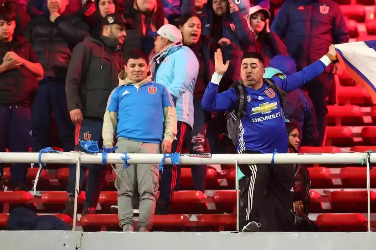 Soccer fans in blue jerseys cheer in the stands of a stadium. Soccer fans in blue jerseys cheer in the stands of a stadium.