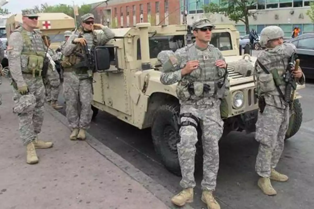 Soldados con uniforme de camuflaje y equipo militar están de pie junto a un vehículo militar en una calle urbana Soldados con uniforme de camuflaje y equipo militar están de pie junto a un vehículo militar en una calle urbana