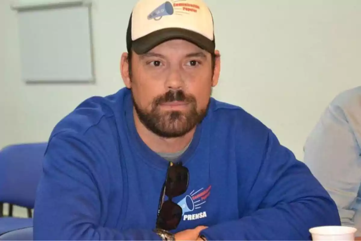 Man with a beard and a white cap sitting at a table wearing a blue sweater with the word Man with a beard and a white cap sitting at a table wearing a blue sweater with the word