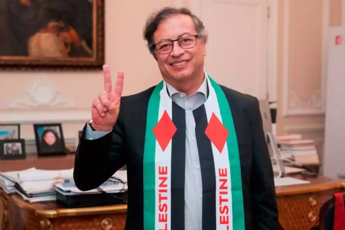 Hombre con gafas y bufanda con los colores de Palestina haciendo el signo de la paz con la mano en una oficina.
