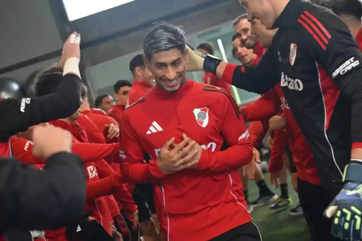 River Plate player smiles as his teammates congratulate and surround him during an indoor training session
