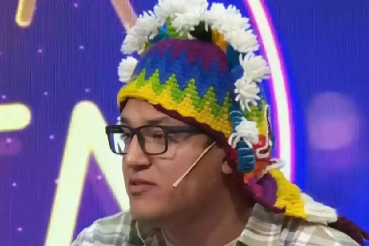 Hombre con gafas y gorro colorido de lana con adornos blancos hablando en un programa de televisión Hombre con gafas y gorro colorido de lana con adornos blancos hablando en un programa de televisión