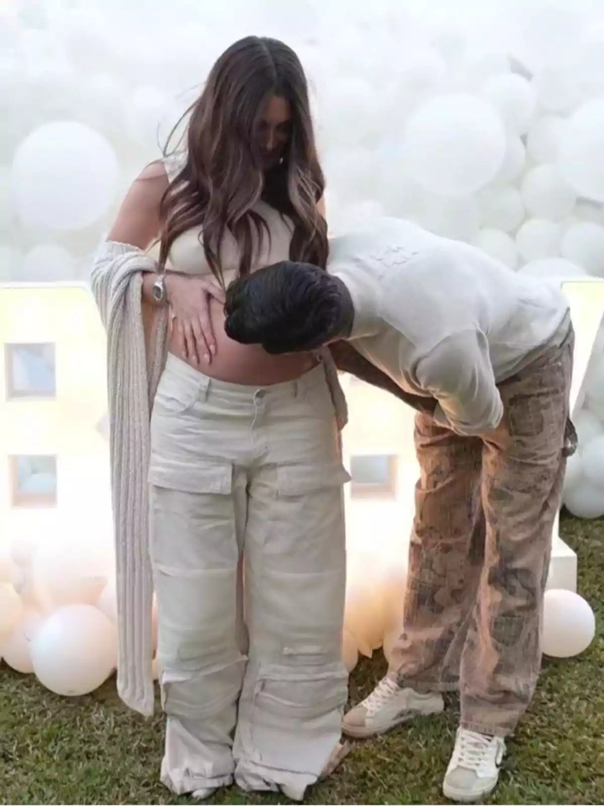 Pareja celebrando un embarazo mientras el hombre besa la barriga de la mujer rodeados de globos blancos Pareja celebrando un embarazo mientras el hombre besa la barriga de la mujer rodeados de globos blancos