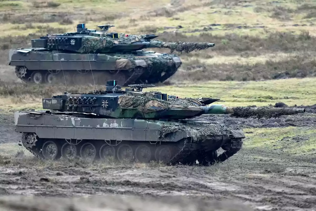 Dos tanques Leopard camuflados avanzan por un terreno fangoso durante un ejercicio militar en campo abierto Dos tanques Leopard camuflados avanzan por un terreno fangoso durante un ejercicio militar en campo abierto