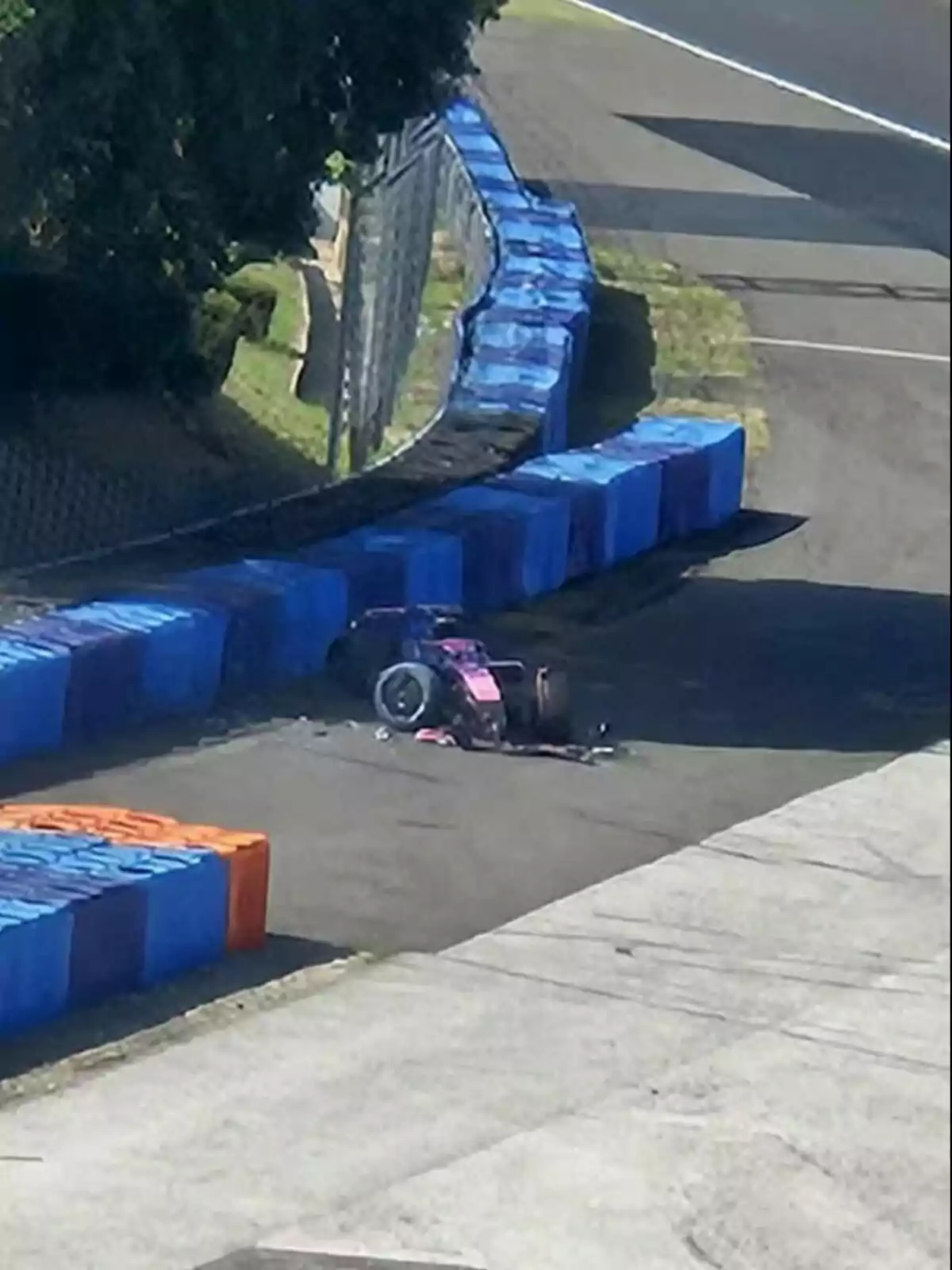 Racing single-seater crashed into a blue and orange safety barrier on a racetrack Racing single-seater crashed into a blue and orange safety barrier on a racetrack