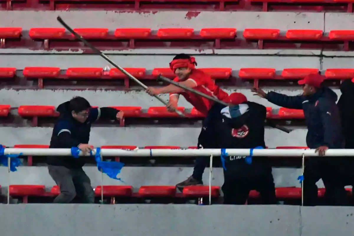 Fans arguing and fighting in the stands of a soccer stadium with red seats Fans arguing and fighting in the stands of a soccer stadium with red seats