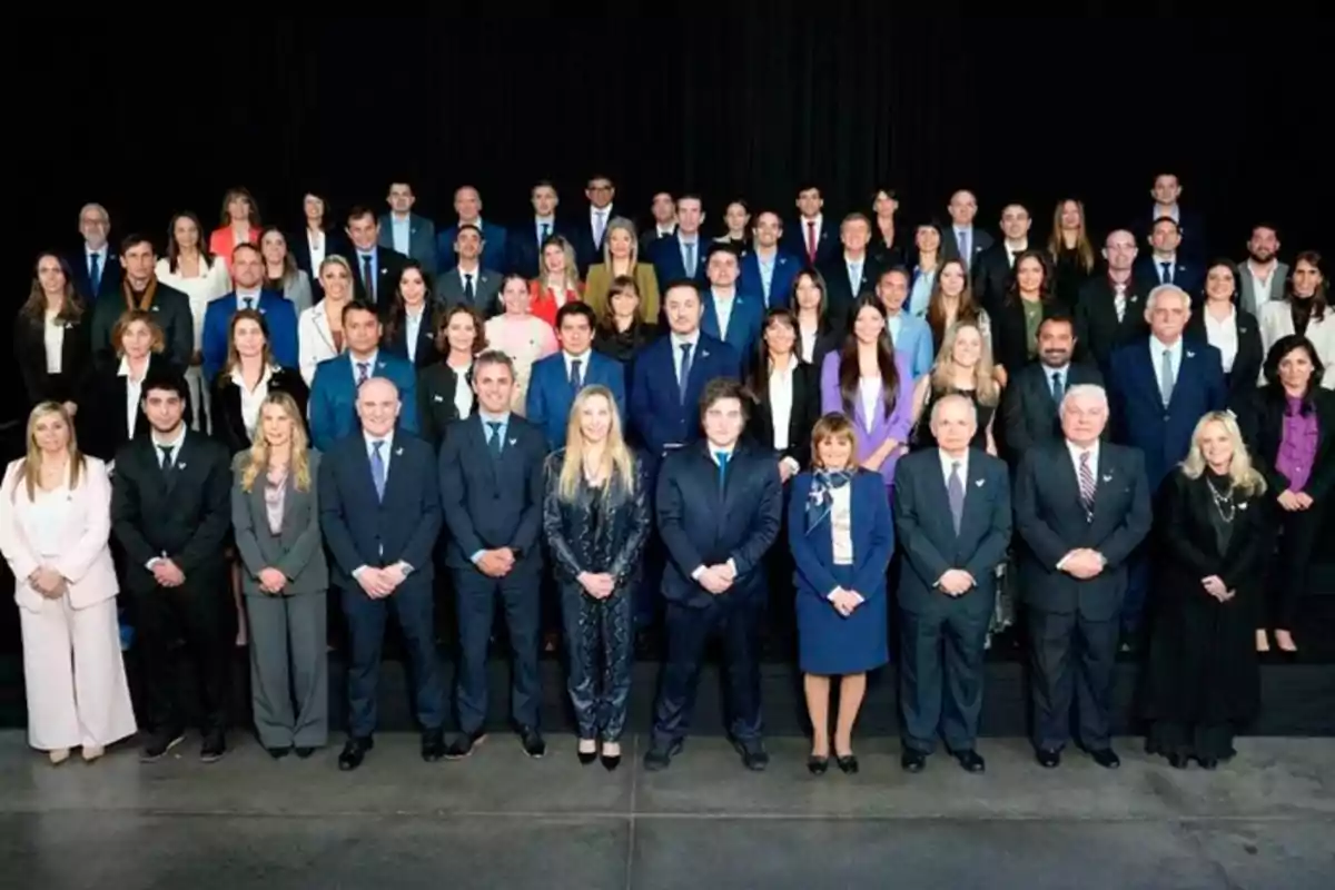 A large group of people dressed formally posing for a group photo against a dark background