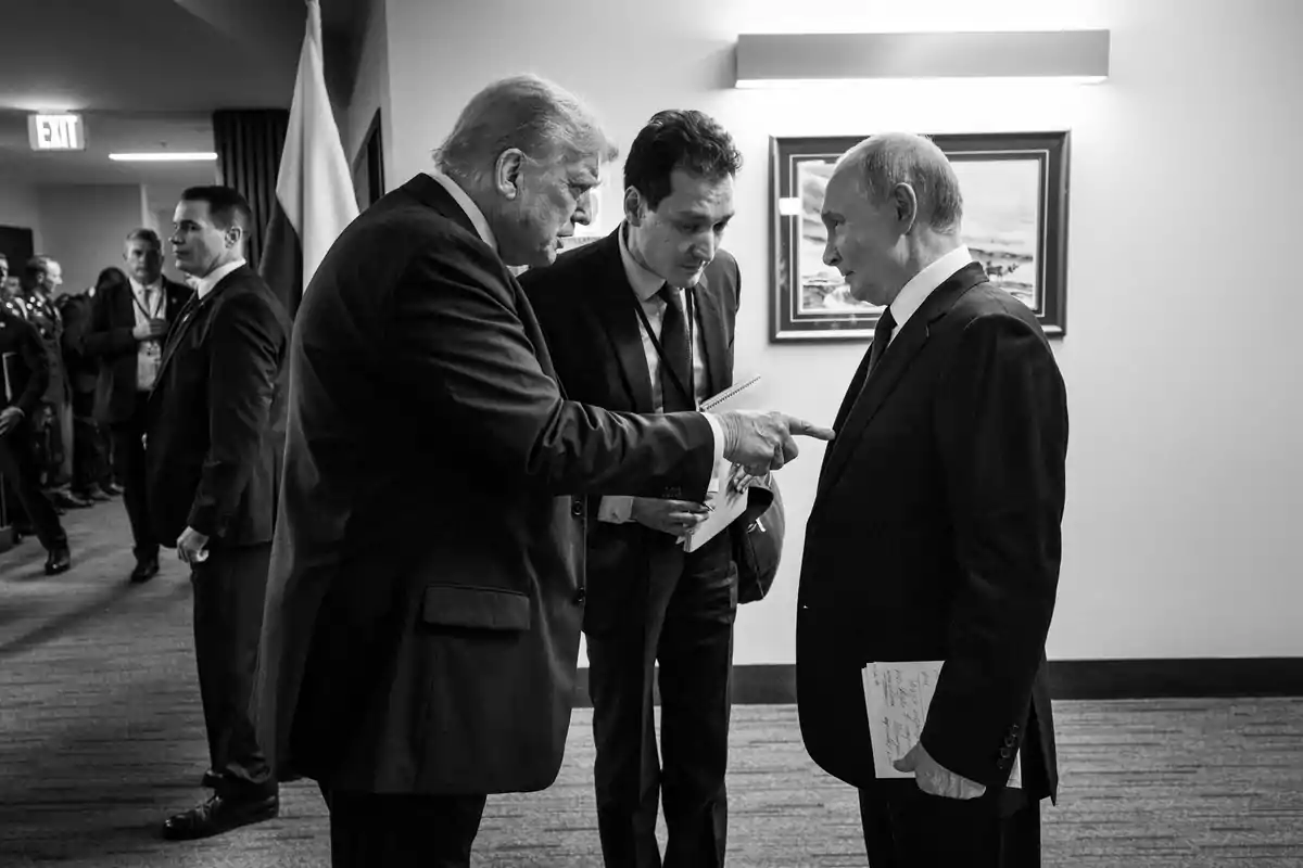 Three men in suits are having a serious conversation in a hallway while one of them points his finger at another.