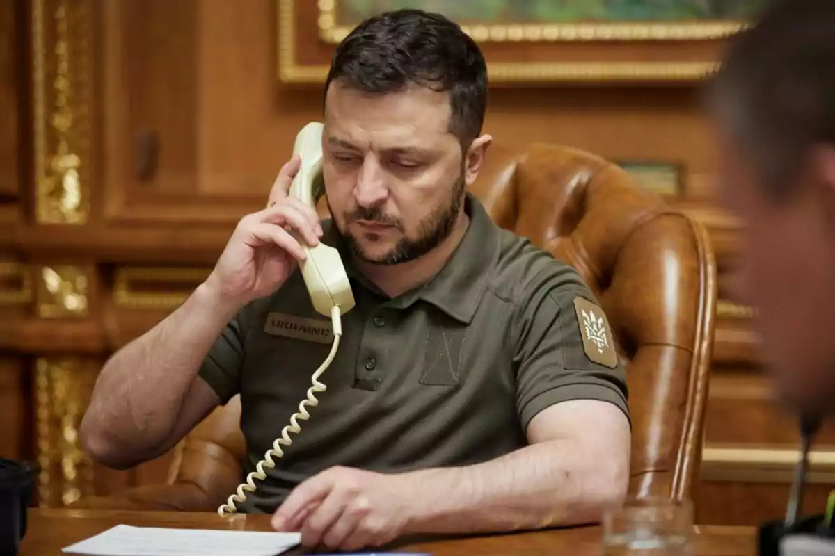 Hombre sentado en un escritorio hablando por teléfono mientras revisa unos documentos en una oficina elegante Hombre sentado en un escritorio hablando por teléfono mientras revisa unos documentos en una oficina elegante