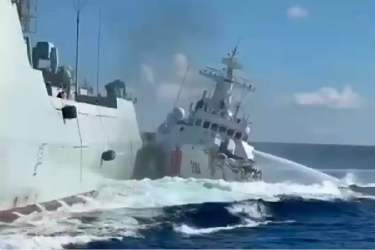 Two ships collide at sea as one of them sprays water at the other under a clear sky.
