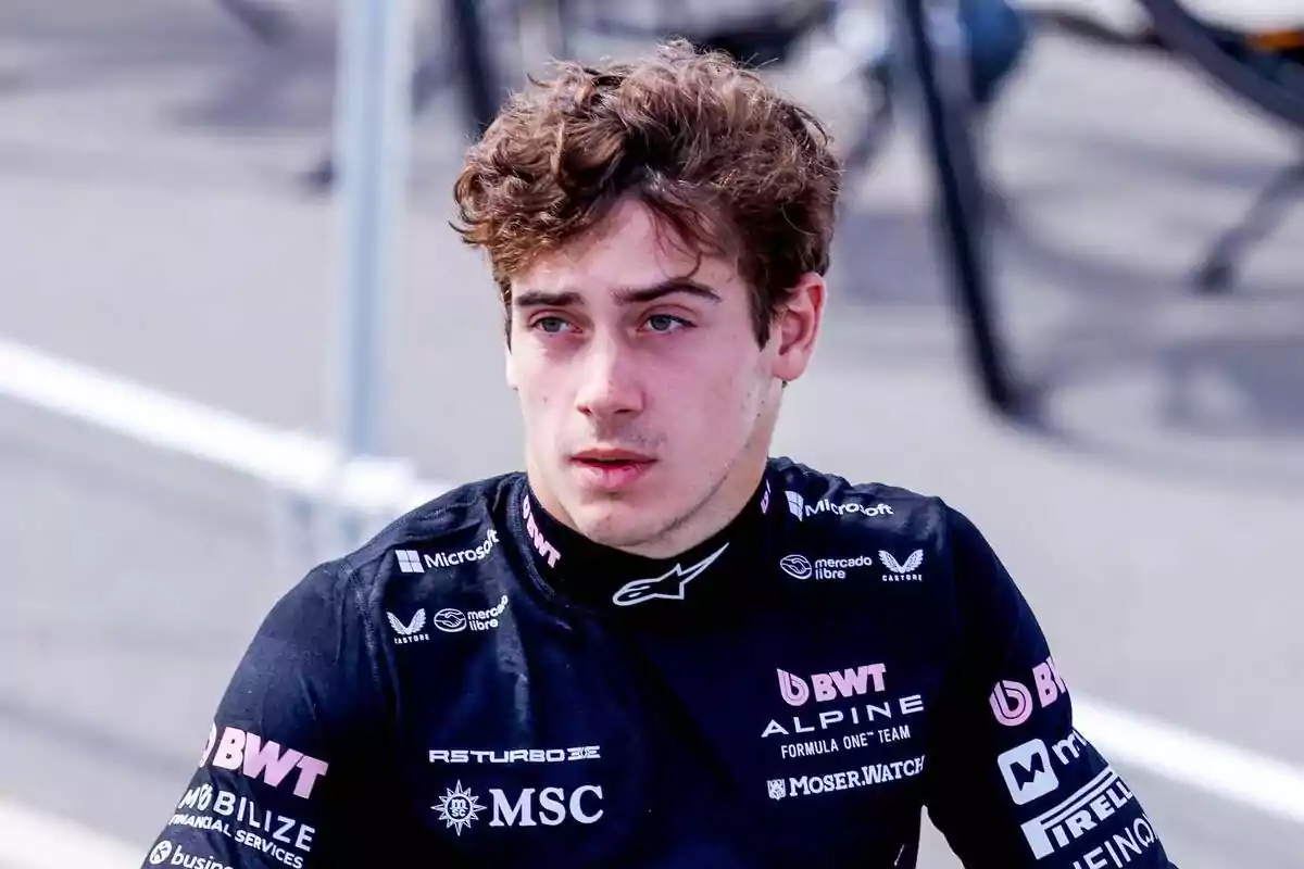 Joven piloto con uniforme de carreras negro de la escudería Alpine en un entorno de paddock