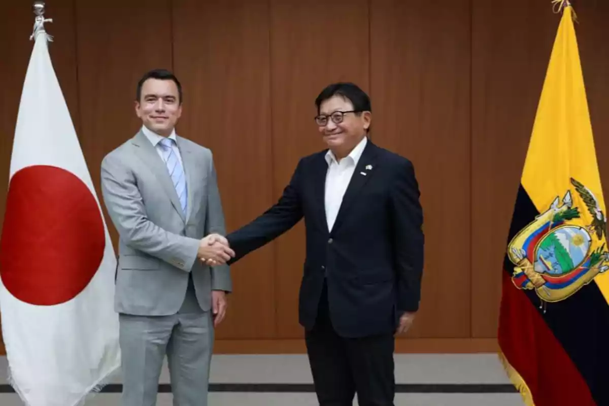 Dos hombres de traje se dan la mano frente a las banderas de Japón y Ecuador