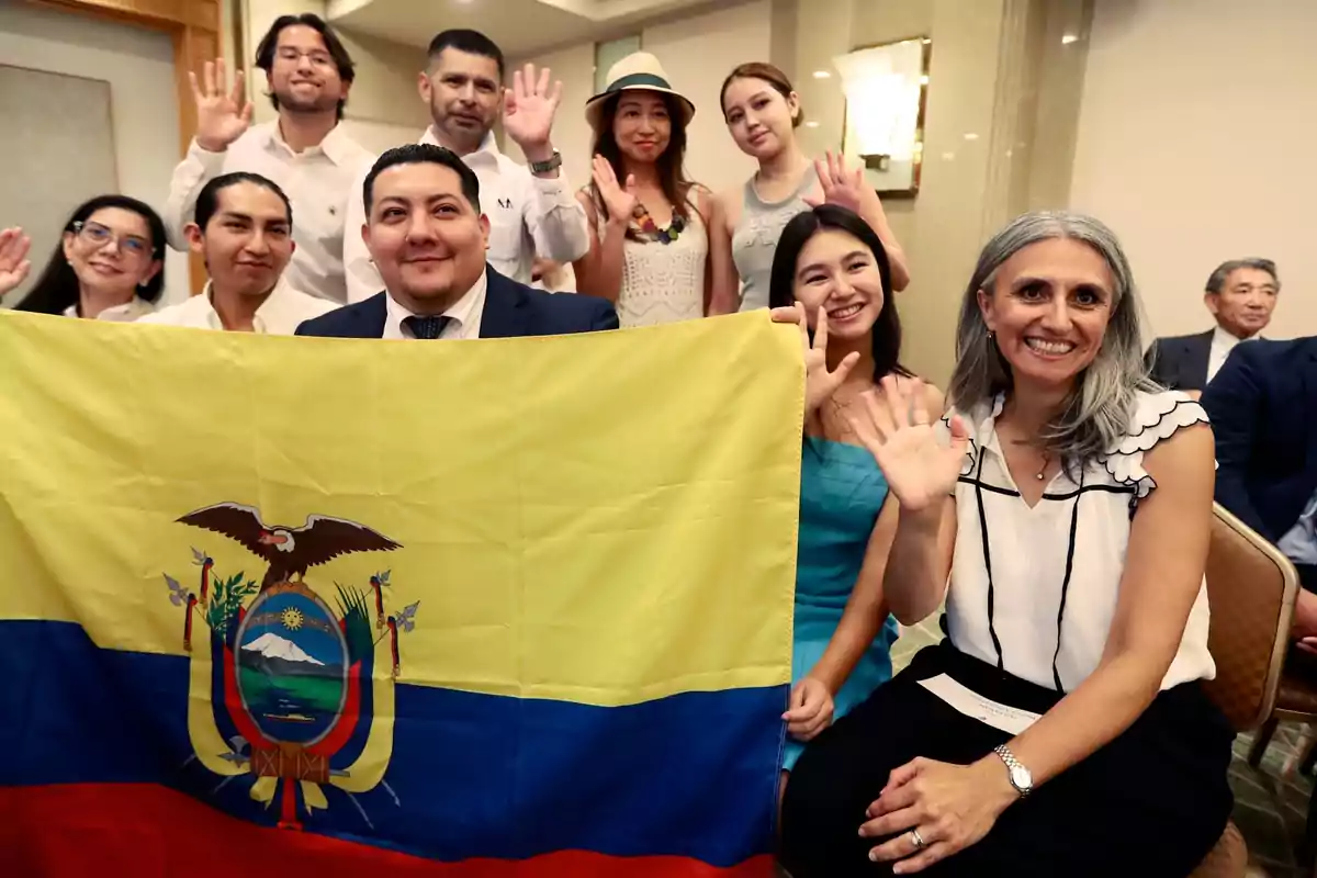 Group of smiling people posing and waving while holding an Ecuadorian flag at an indoor event Group of smiling people posing and waving while holding an Ecuadorian flag at an indoor event