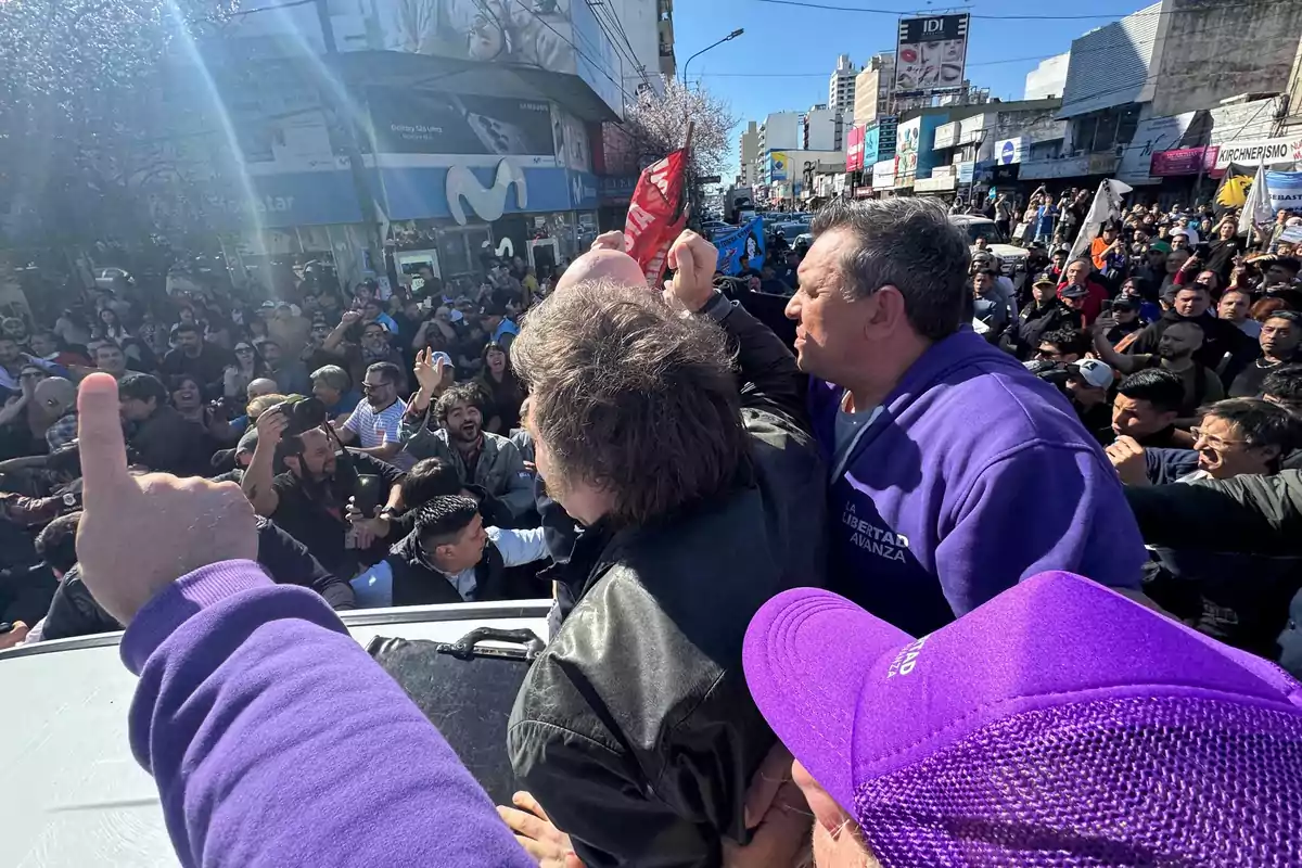 Crowd gathered at a political rally in a city, with people raising flags and wearing clothing with messages of support