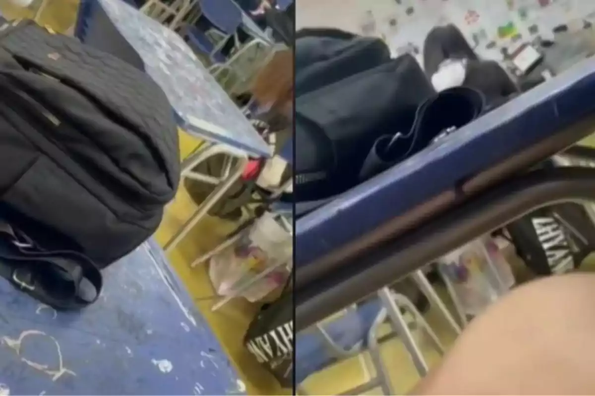 Dos escritorios escolares azules con mochilas negras encima en un salón de clases, al fondo se ven más pupitres y una persona sentada Dos escritorios escolares azules con mochilas negras encima en un salón de clases, al fondo se ven más pupitres y una persona sentada