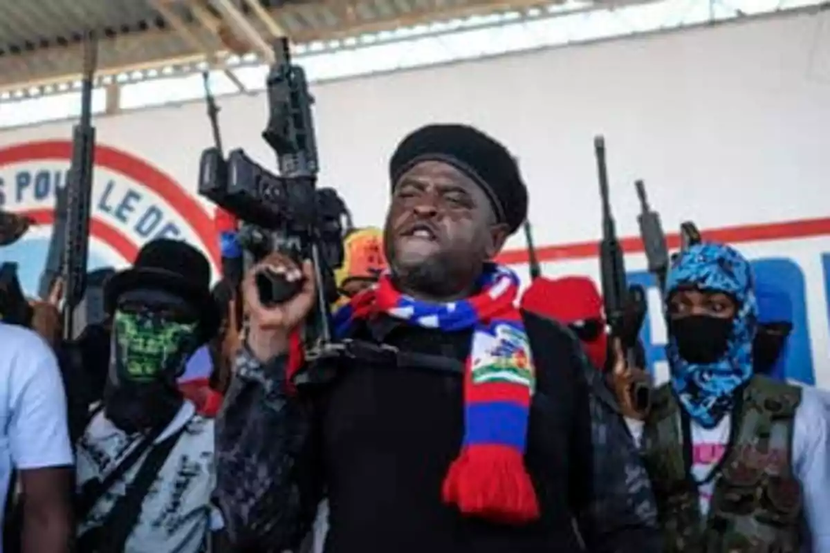 Un grupo de hombres armados con rifles y vestimenta llamativa se encuentra reunido en un espacio cubierto, uno de ellos al frente lleva una bufanda de colores rojo, azul y blanco Un grupo de hombres armados con rifles y vestimenta llamativa se encuentra reunido en un espacio cubierto, uno de ellos al frente lleva una bufanda de colores rojo, azul y blanco