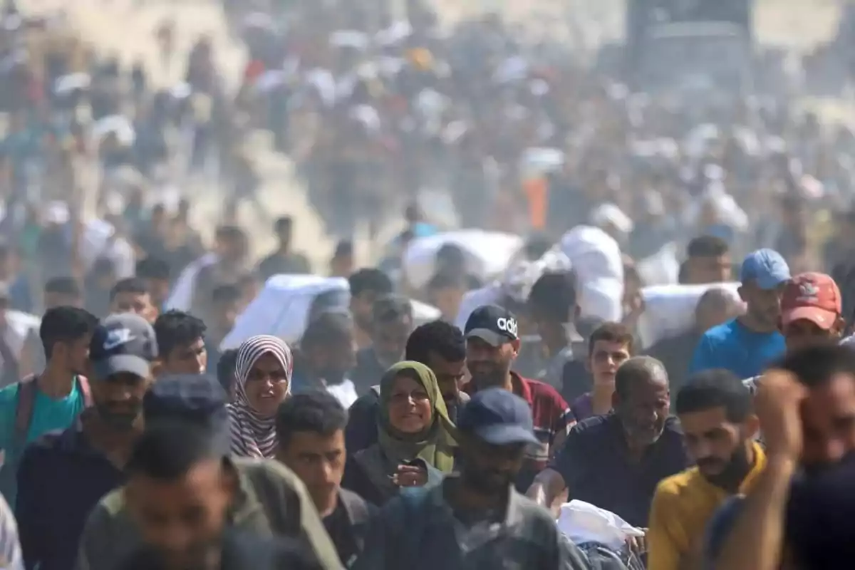 Multitud de personas caminando en una situación de emergencia cargando pertenencias y con expresiones de preocupación Multitud de personas caminando en una situación de emergencia cargando pertenencias y con expresiones de preocupación