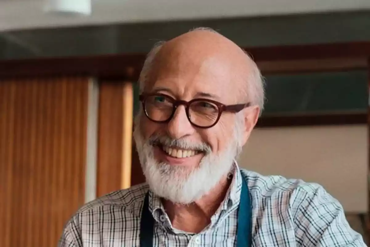 Older man with a white beard and glasses smiling while wearing a plaid jersey and a blue apron Older man with a white beard and glasses smiling while wearing a plaid jersey and a blue apron