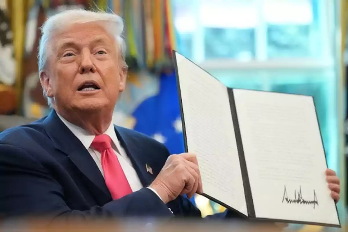 Gray-haired man with a pink tie showing an open document with a visible signature at the bottom