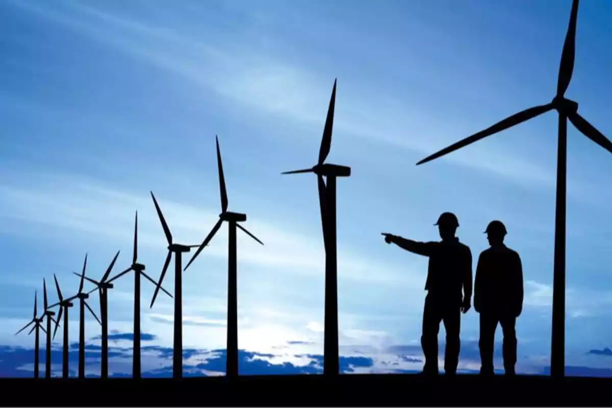 Dos personas con casco observan y supervisan un parque eólico con varios aerogeneradores al atardecer Dos personas con casco observan y supervisan un parque eólico con varios aerogeneradores al atardecer