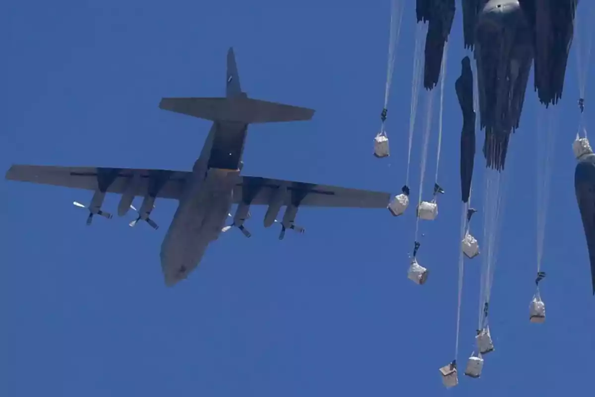 Avión militar lanzando suministros con paracaídas en el cielo azul Avión militar lanzando suministros con paracaídas en el cielo azul