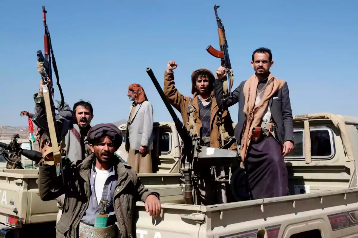Grupo de hombres armados con rifles y vestimenta tradicional de pie en la parte trasera de una camioneta bajo un cielo despejado Grupo de hombres armados con rifles y vestimenta tradicional de pie en la parte trasera de una camioneta bajo un cielo despejado