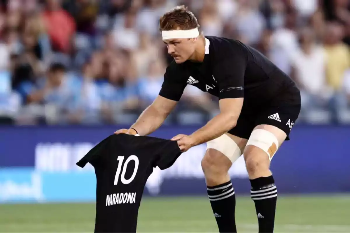 Rugby player in a black uniform holds a jersey with the number 10 and the name Maradona in a stadium full of spectators. Rugby player in a black uniform holds a jersey with the number 10 and the name Maradona in a stadium full of spectators.