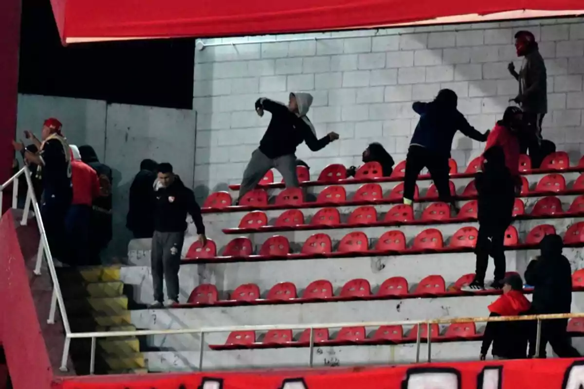 Fans in the stands of a stadium engage in a fight, throwing objects and displaying aggressive behavior. Fans in the stands of a stadium engage in a fight, throwing objects and displaying aggressive behavior.
