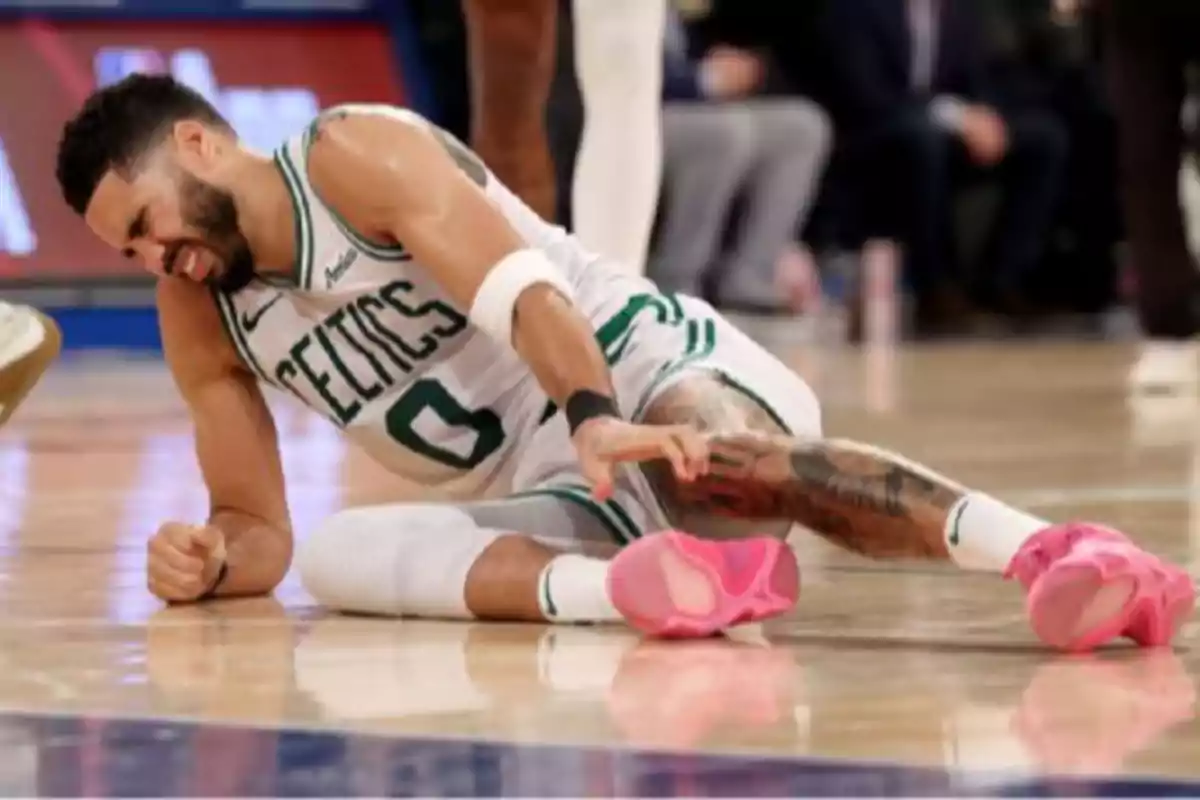 Jugador de baloncesto de los Celtics en el suelo con gesto de dolor sujetándose la pierna durante un partido Jugador de baloncesto de los Celtics en el suelo con gesto de dolor sujetándose la pierna durante un partido