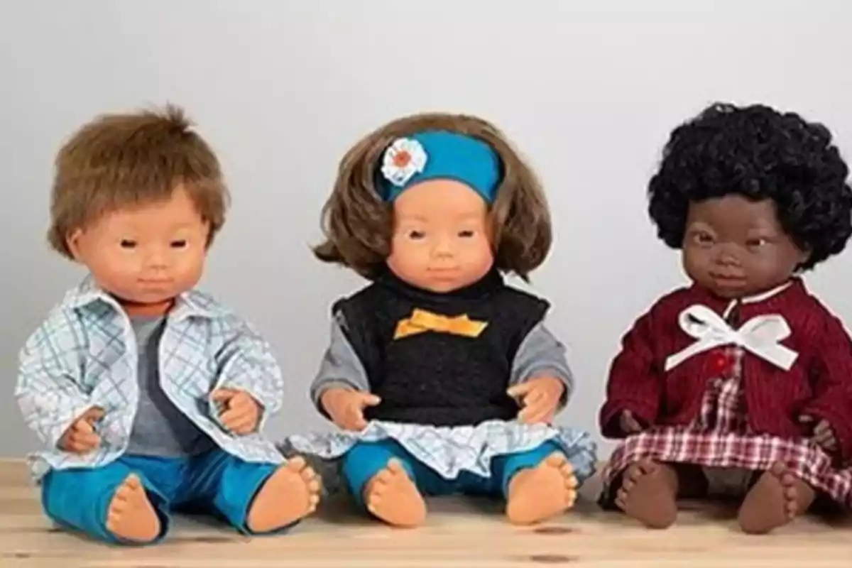 Three dolls sitting on a wooden surface, each with a different skin tone and colorful clothing