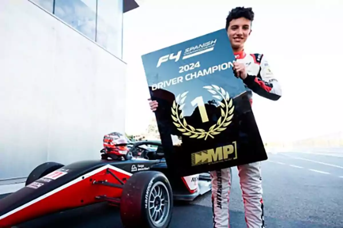 Smiling race car driver holds a large champion sign next to a single-seater race car on a track Smiling race car driver holds a large champion sign next to a single-seater race car on a track