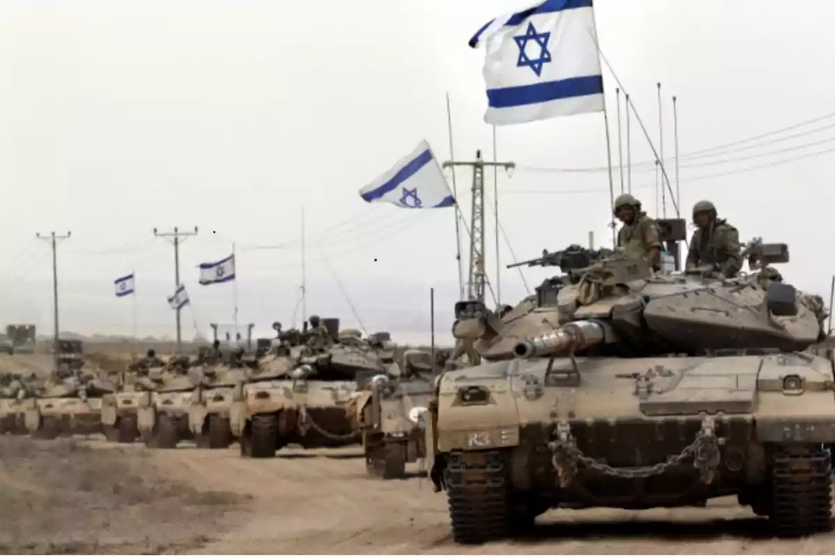 Tanques militares israelíes avanzan por un camino de tierra con soldados a bordo y banderas de Israel ondeando Tanques militares israelíes avanzan por un camino de tierra con soldados a bordo y banderas de Israel ondeando