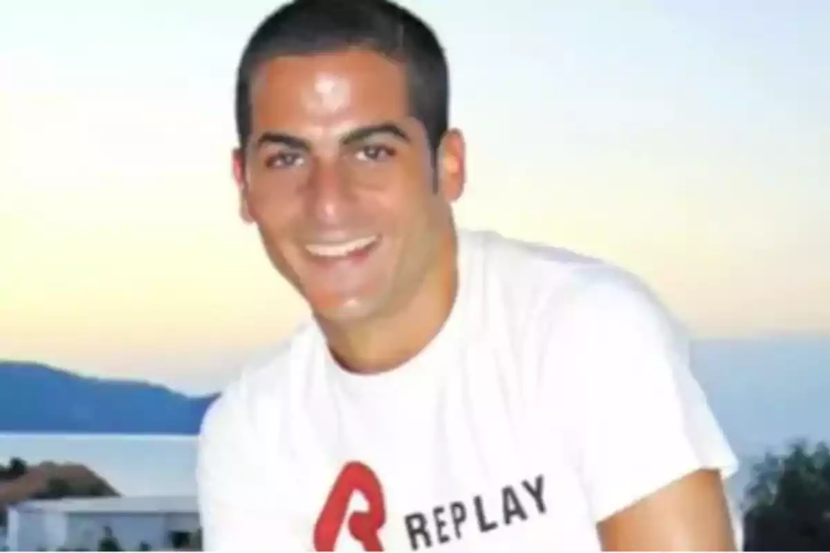 Joven sonriente con camiseta blanca de la marca Replay al aire libre con paisaje de fondo