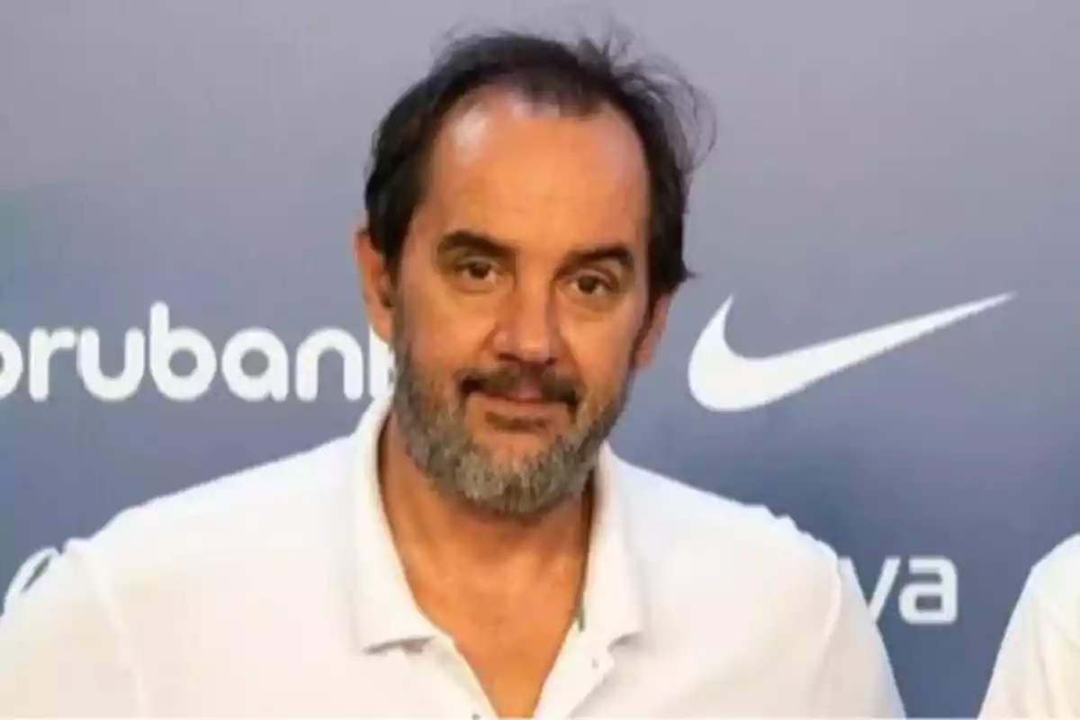 Middle-aged man with a beard and dark hair is wearing a white polo jersey and is standing in front of a background with sports brand logos. Middle-aged man with a beard and dark hair is wearing a white polo jersey and is standing in front of a background with sports brand logos.