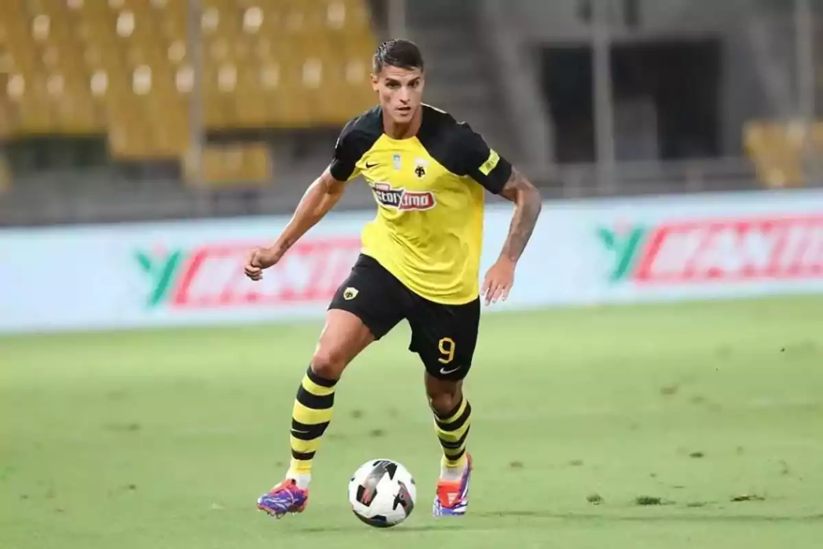 Futbolista con uniforme amarillo y negro controla el balón en un estadio durante un partido Futbolista con uniforme amarillo y negro controla el balón en un estadio durante un partido