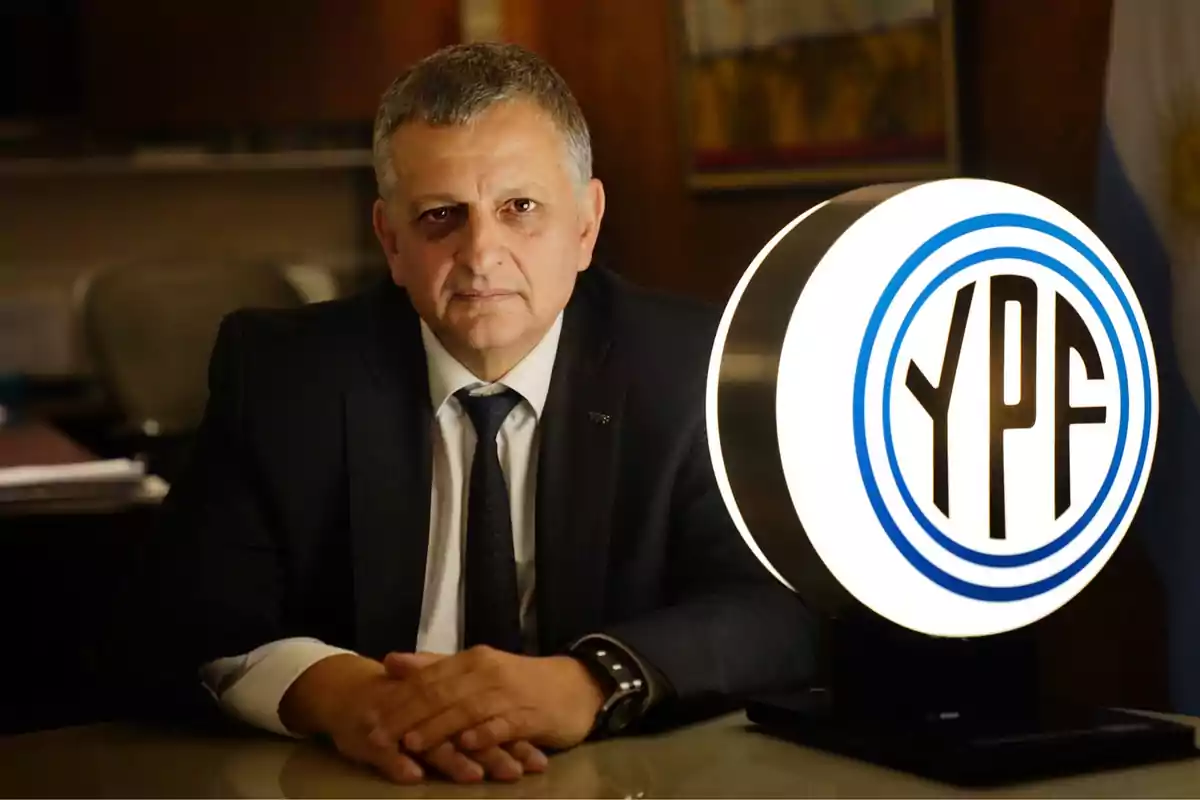 Man in a suit sitting in an office next to an illuminated YPF logo Man in a suit sitting in an office next to an illuminated YPF logo