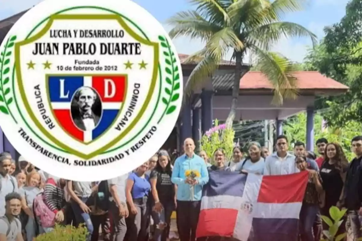 Grupo de personas posando al aire libre con una bandera de República Dominicana y un escudo grande de la organización Lucha y Desarrollo Juan Pablo Duarte en primer plano