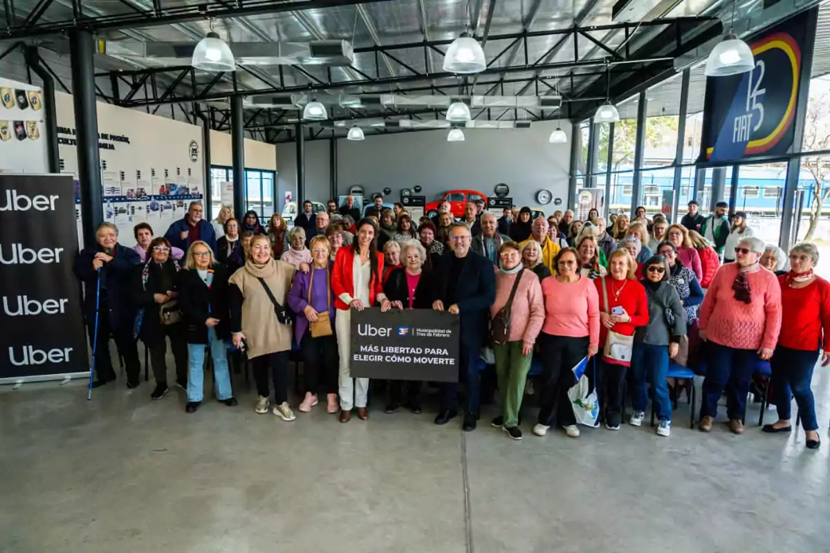 Un grupo numeroso de personas mayores posa sonriente en el interior de un edificio moderno junto a un cartel de Uber que promueve la libertad de movimiento Un grupo numeroso de personas mayores posa sonriente en el interior de un edificio moderno junto a un cartel de Uber que promueve la libertad de movimiento