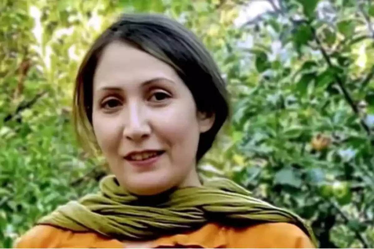 Mujer de cabello oscuro con bufanda verde y blusa naranja sonriendo al aire libre con árboles de fondo Mujer de cabello oscuro con bufanda verde y blusa naranja sonriendo al aire libre con árboles de fondo