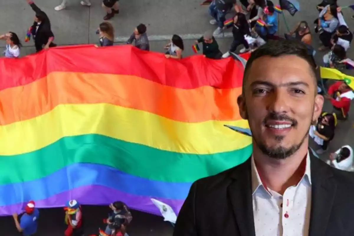 Hombre sonriente con barba y saco oscuro frente a una bandera arcoíris en una marcha del orgullo LGBTQ+ Hombre sonriente con barba y saco oscuro frente a una bandera arcoíris en una marcha del orgullo LGBTQ+