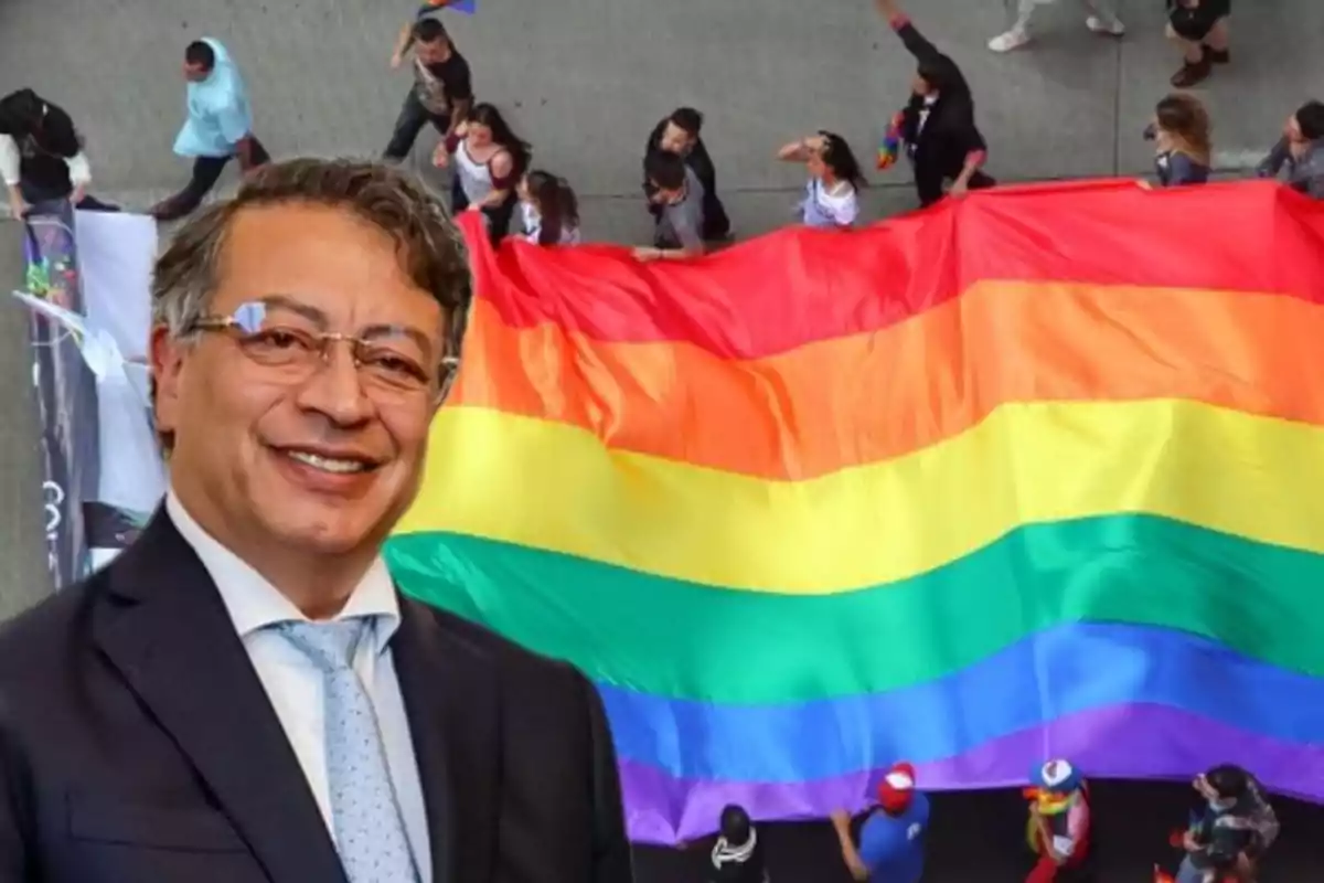 Hombre con gafas y traje sonriente al frente de una marcha con una gran bandera arcoíris ondeando detrás de él